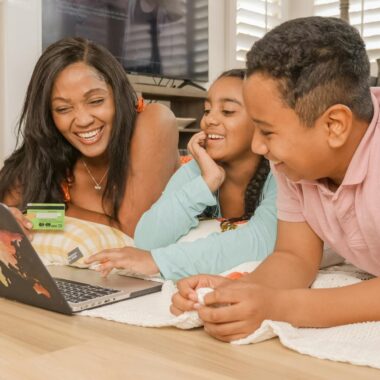 A happy family of three enjoying online shopping together on a laptop in a cozy living room.