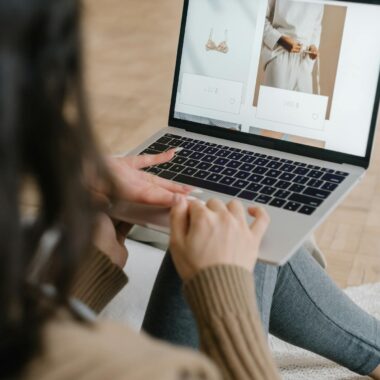 Female browsing an online fashion store on a laptop indoors, focusing on clothing and accessories.